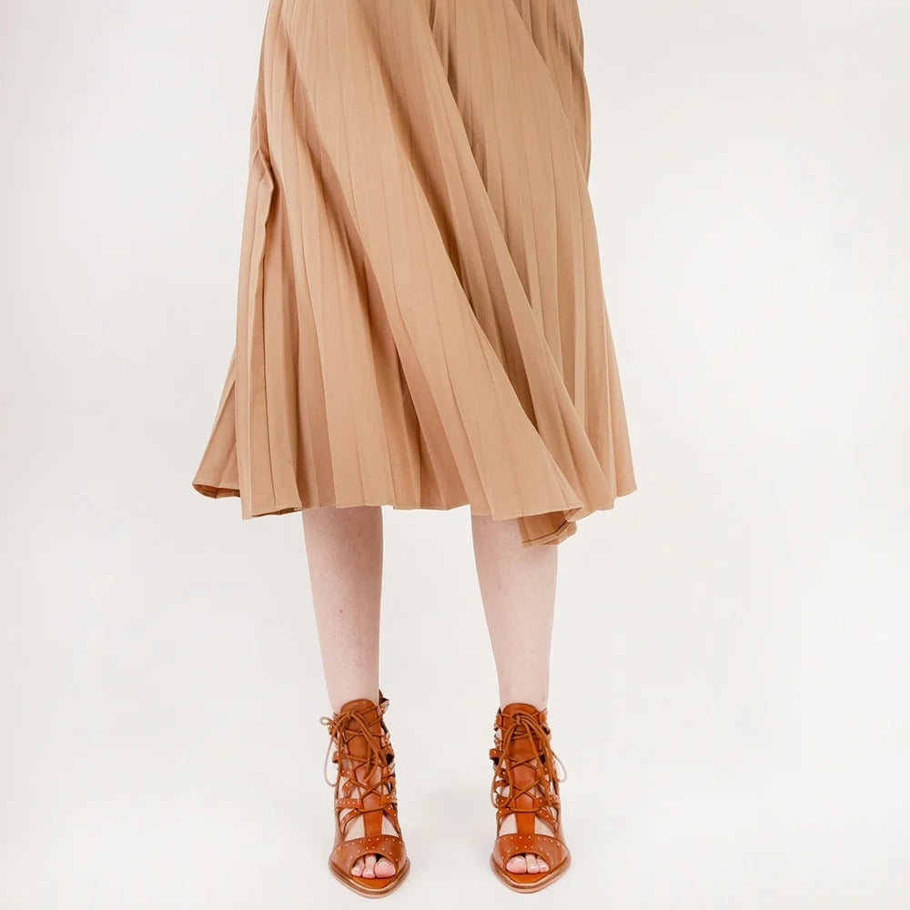 Lace Up Booties In Calfskin from House of Hide in brown calfskin leather with strappy lace-up heeled design being worn with tan pleated midi skirt against light background