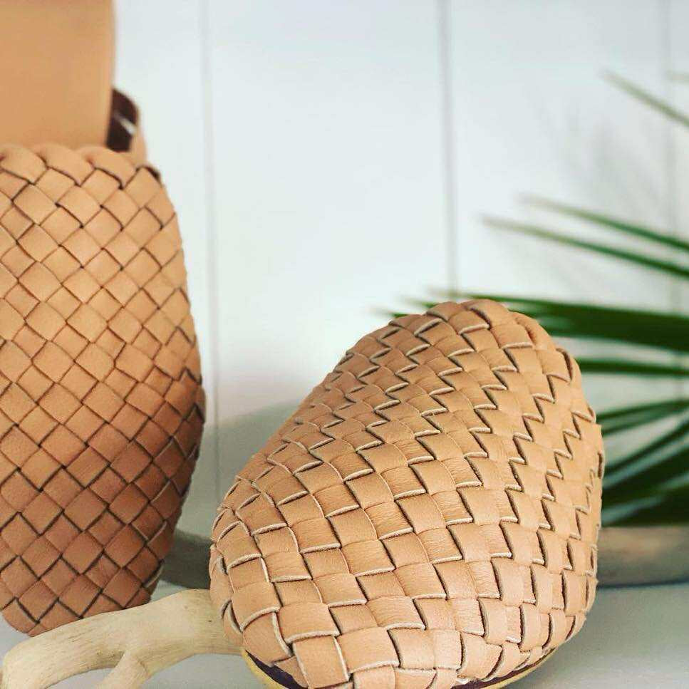 Woven pineapple-shaped object on a white surface with a blurred green plant in the background