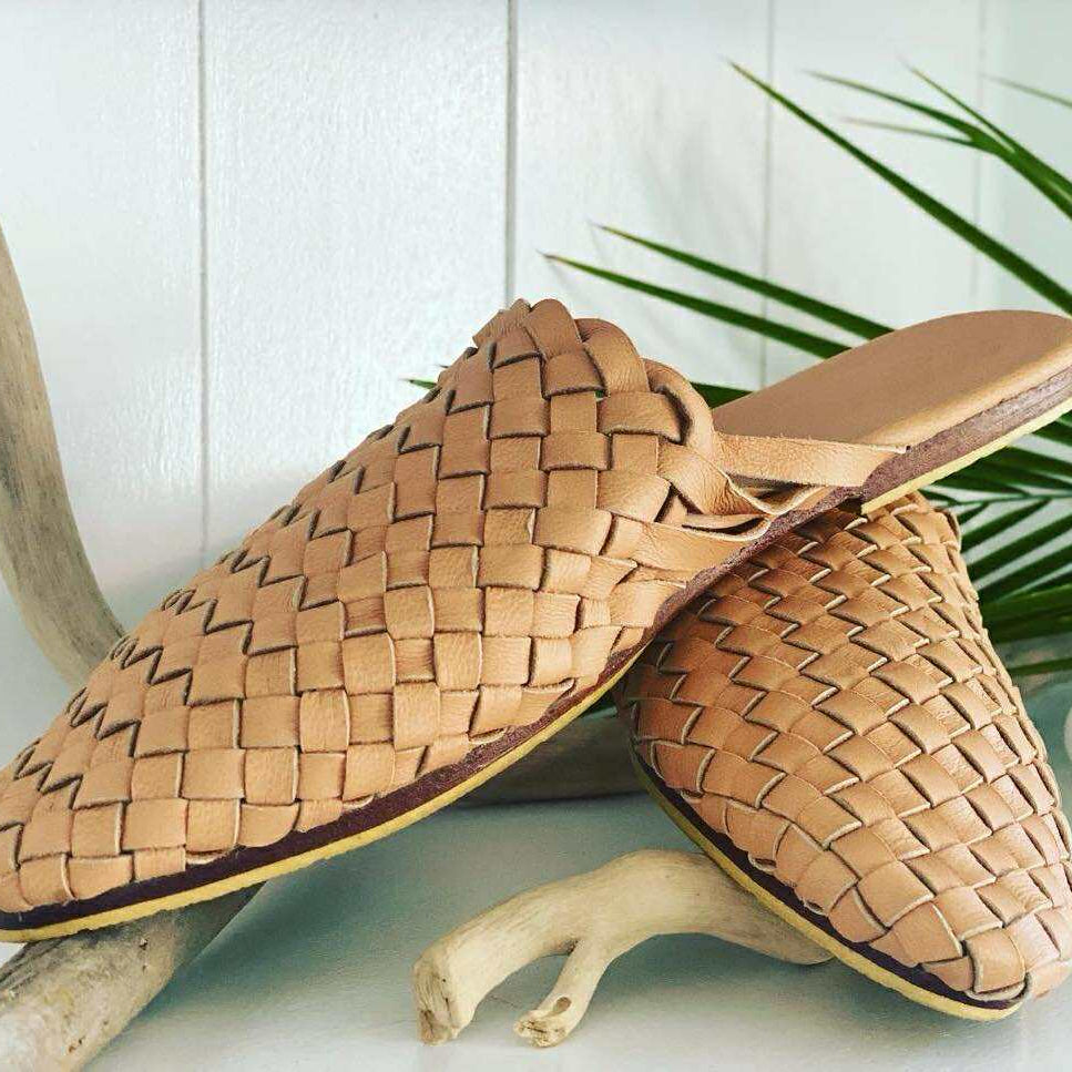 Pair of woven tan shoes on a white surface with a plant in the background