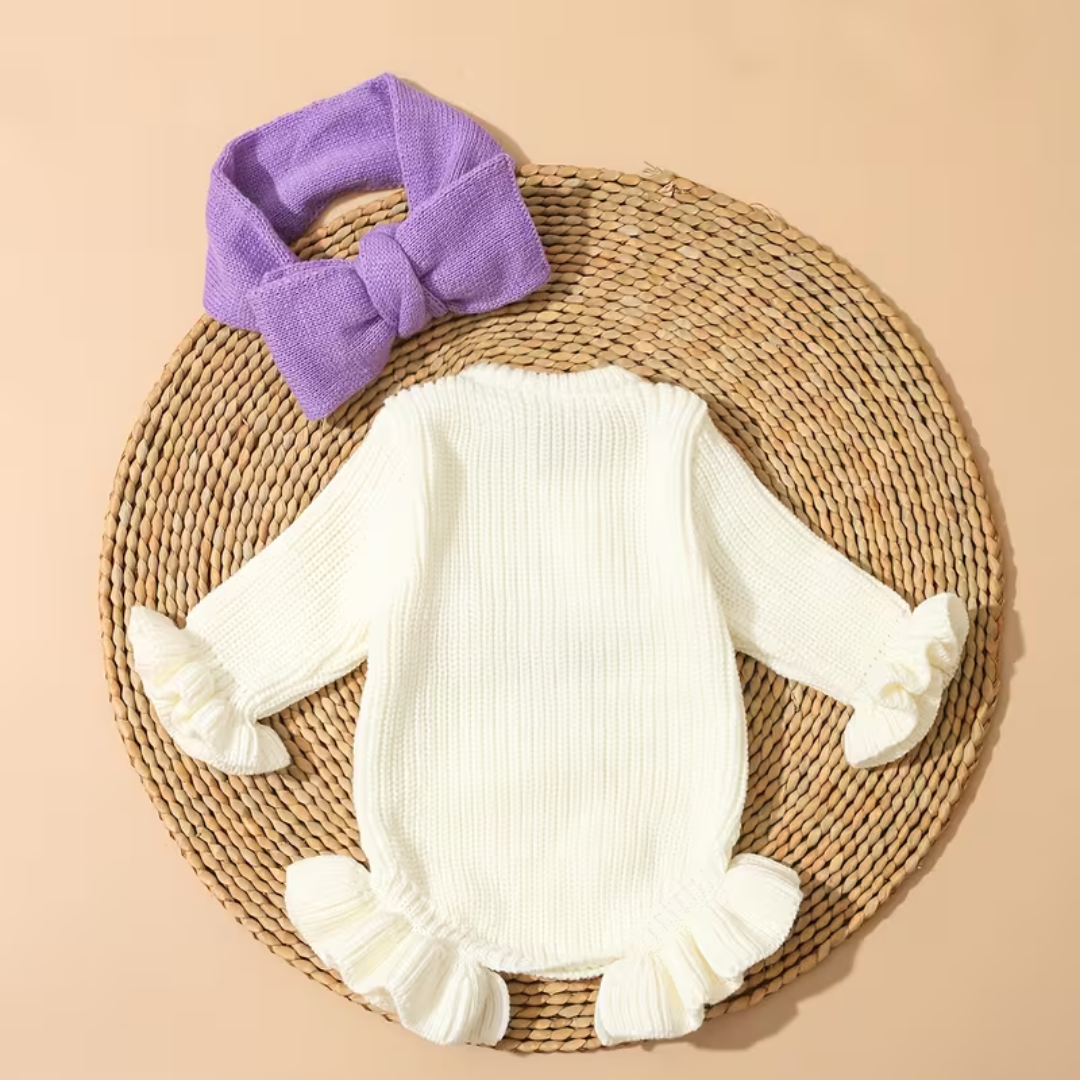 Little Darling Knit Romper Set from House of Hide in cream ribbed knit with gentle stretch, ruffled trim at cuffs and leg openings, violet embroidered bow graphic, matching violet bow headband accessory on circular woven display