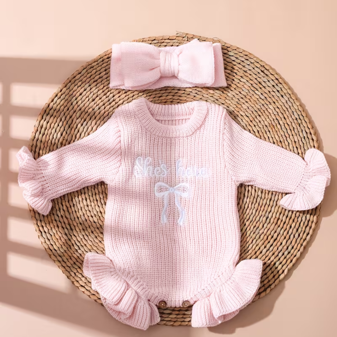 Little Darling Knit Romper Set from House of Hide in soft pale pink ribbed knit long-sleeve romper with ruffled trim, embroidered bow, coordinating pale pink bow headband being styled on round woven placemat with dreamy backdrop