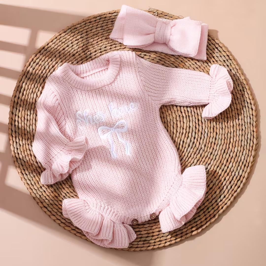 Little Darling Knit Romper Set from House of Hide in pale pink gentle ribbed knit with button closure for easy diaper changes, ruffled leg openings, embroidered bow detail, matching pale pink bow headband on woven circular display