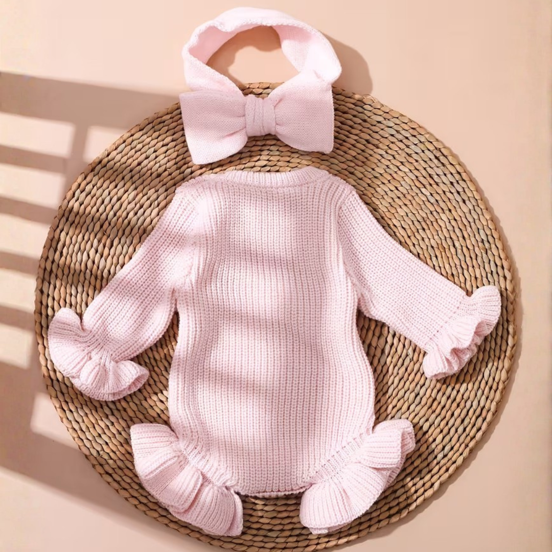 Little Darling Knit Romper Set from House of Hide in delicate pale pink chunky ribbed knit romper with ruffled edges, embroidered bow graphic, soft stretch fabric, coordinated pale pink bow headband being displayed on round woven mat