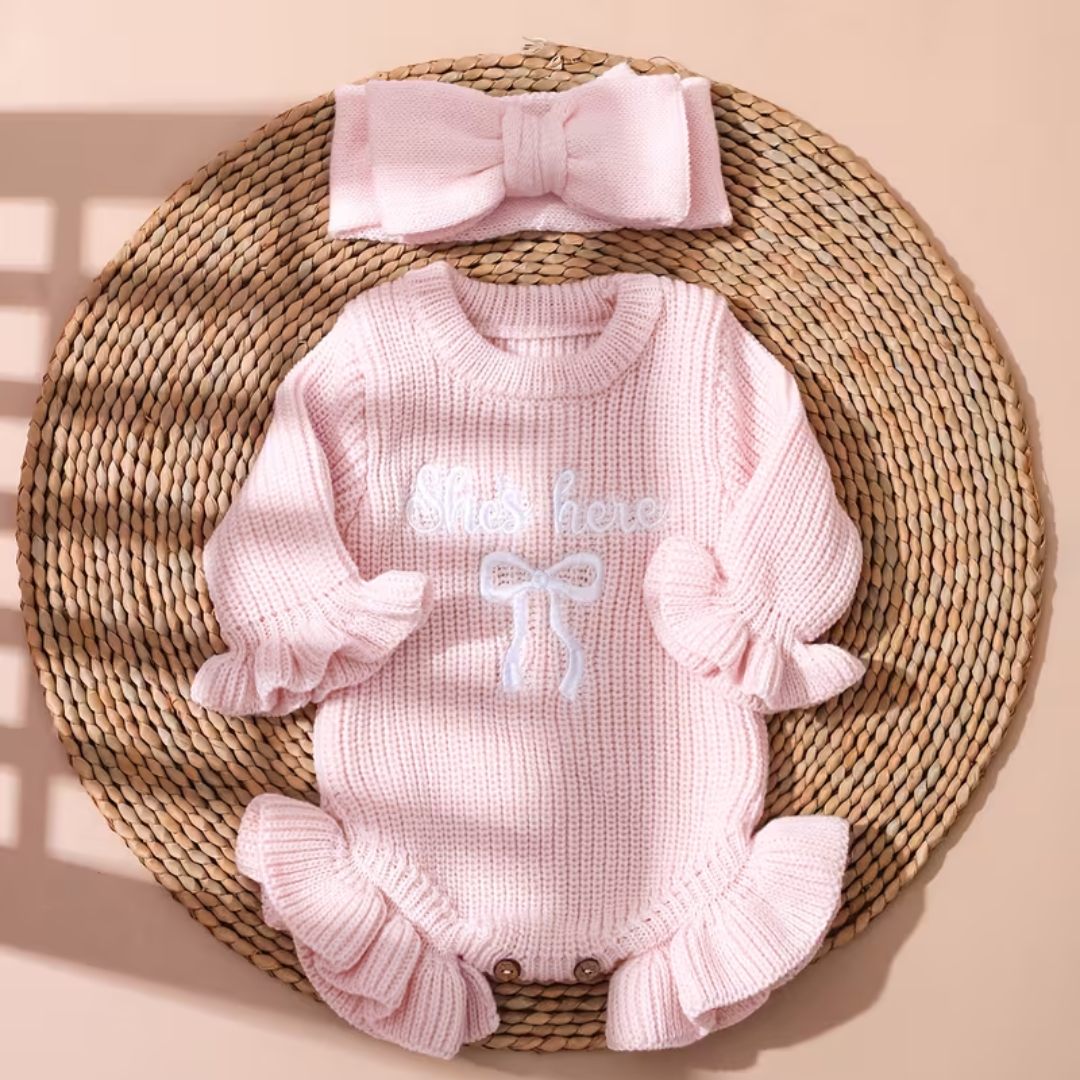 Little Darling Knit Romper Set from House of Hide in pale pink ribbed knit with embroidered bow detail, ruffled cuffs and hem for gentle movement, button closure functionality, matching pale pink bow headband accessory on woven surface