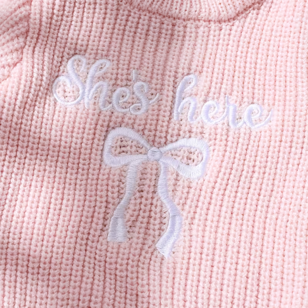 Little Darling Knit Romper Set from House of Hide in soft pale pink ribbed knit baby romper with ruffled trim, embroidered bow accent, gentle on newborn skin, coordinating pale pink bow headband being styled on round woven mat backdrop