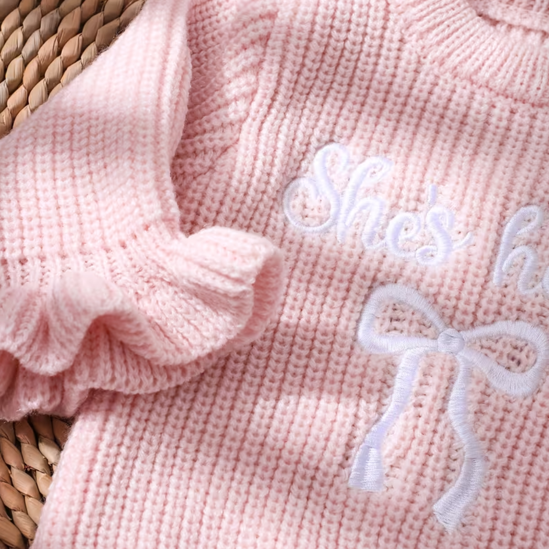 Little Darling Knit Romper Set from House of Hide in pale pink chunky ribbed knit with stretch, ruffled leg openings, embroidered bow design, button closure for easy changes, matching pale pink bow headband on circular woven display