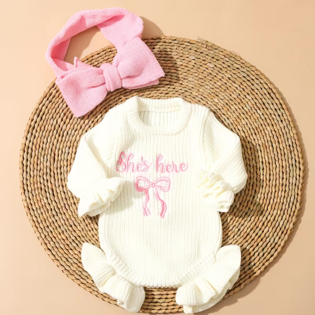 Little Darling Knit Romper Set from House of Hide in soft off-white chunky ribbed knit with pink embroidered text and bow graphic, button closure for easy changes, matching pink bow headband being styled on circular woven placemat