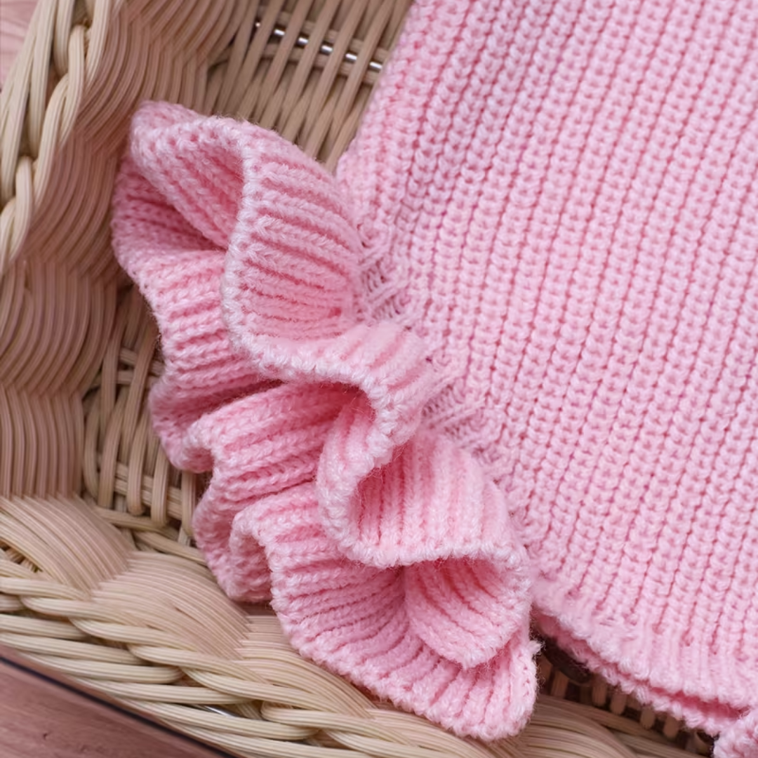 Little Darling Knit Romper Set from House of Hide in pink ribbed knit baby romper with ruffled detailing and white she's here embroidery, coordinating pink bow headband being displayed in wicker basket on wooden plank flooring