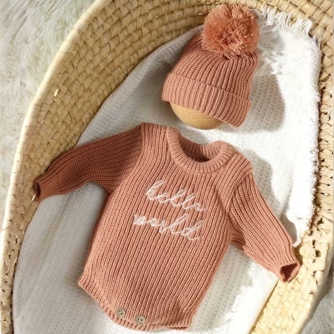 Little Wrangler Knit Romper Set from House of Hide in dusty rose ribbed knit long-sleeve sweater with matching pom-pom beanie being displayed inside woven basket on white blanket
