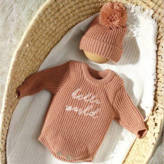Little Wrangler Knit Romper Set from House of Hide in dusty rose ribbed knit long-sleeve sweater with matching pom-pom beanie being displayed inside woven basket on white blanket