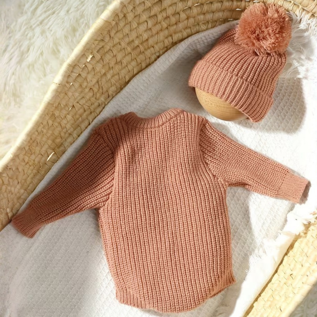 Little Wrangler Knit Romper Set from House of Hide in dusty rose ribbed knit long-sleeve sweater with matching pom-pom beanie being displayed on white blanket inside woven basket
