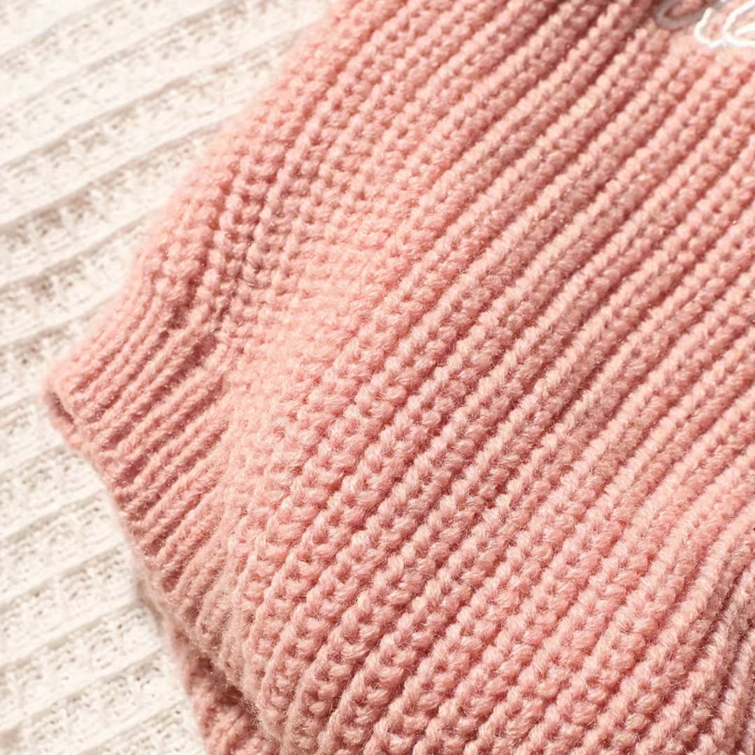 Little Wrangler Knit Romper Set from House of Hide in dusty pink ribbed knit being displayed in close-up over textured off-white knit surface