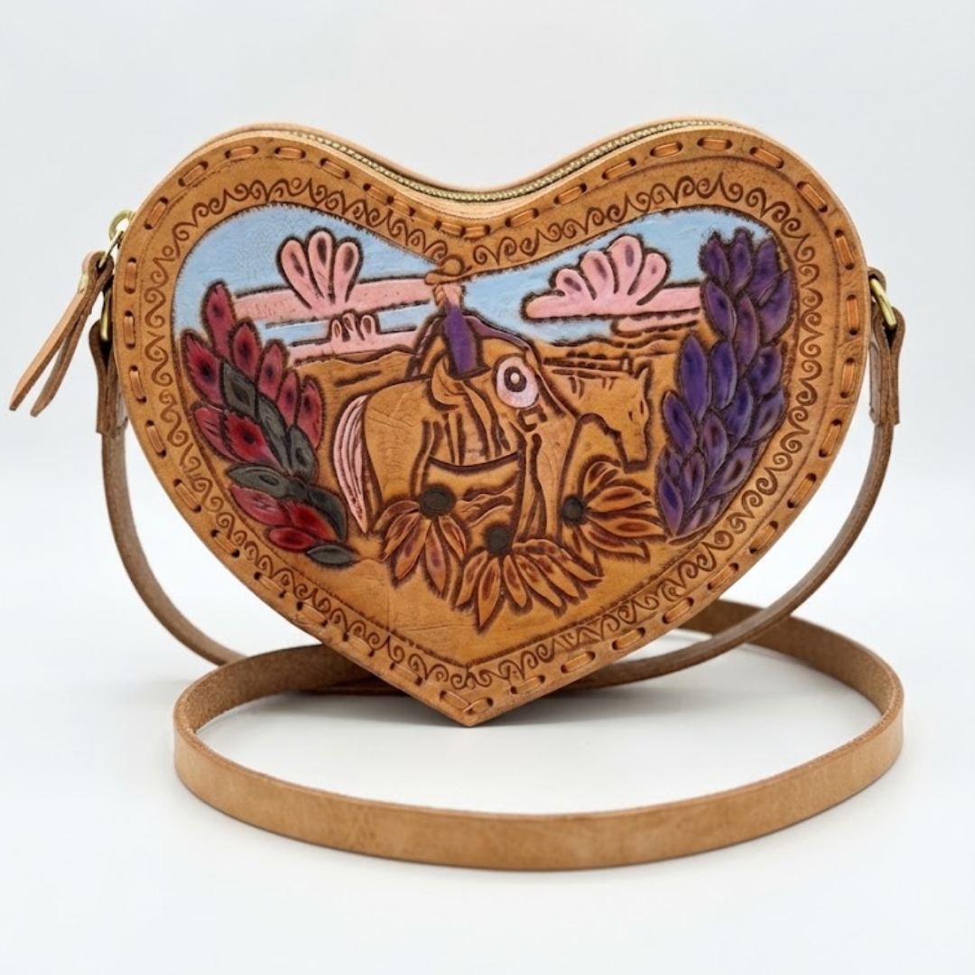 A heart-shaped brown leather crossbody bag with a colorful hand-painted illustration of a cowboy on a horse, set against a plain white background.