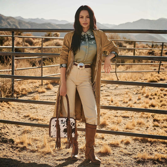 Woman in western attire standing in a desert landscape with mountains in the background