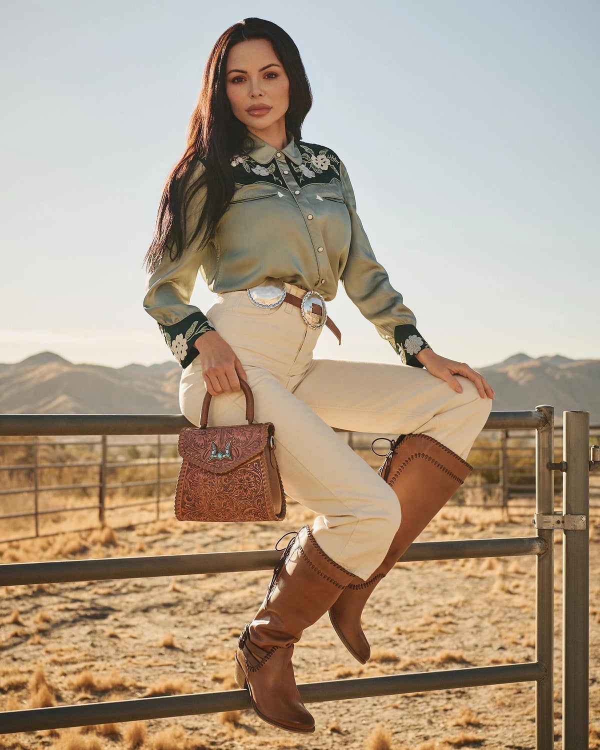 Model showcasing House of Hide women's western fashion with a genuine leather brown handbag in a desert landscape setting