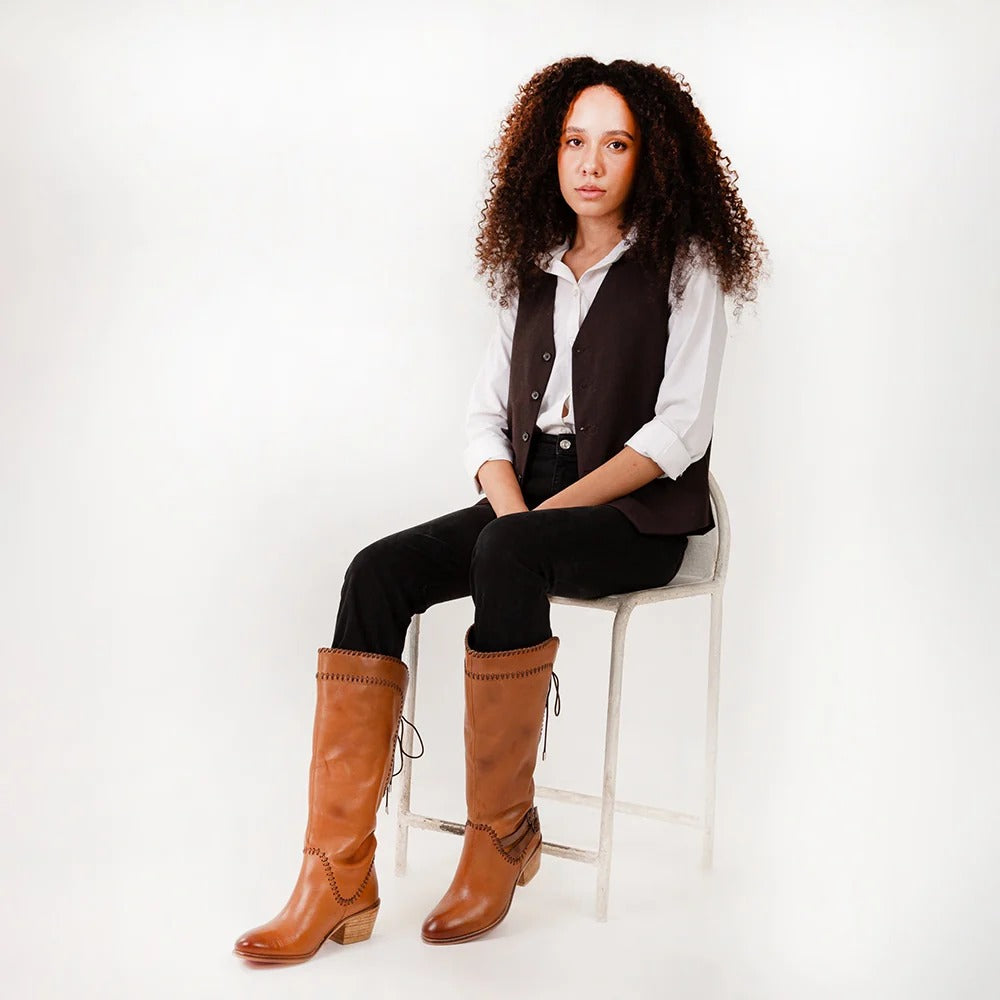 Woman wearing brown knee-high boots sitting on a white stool against a white background