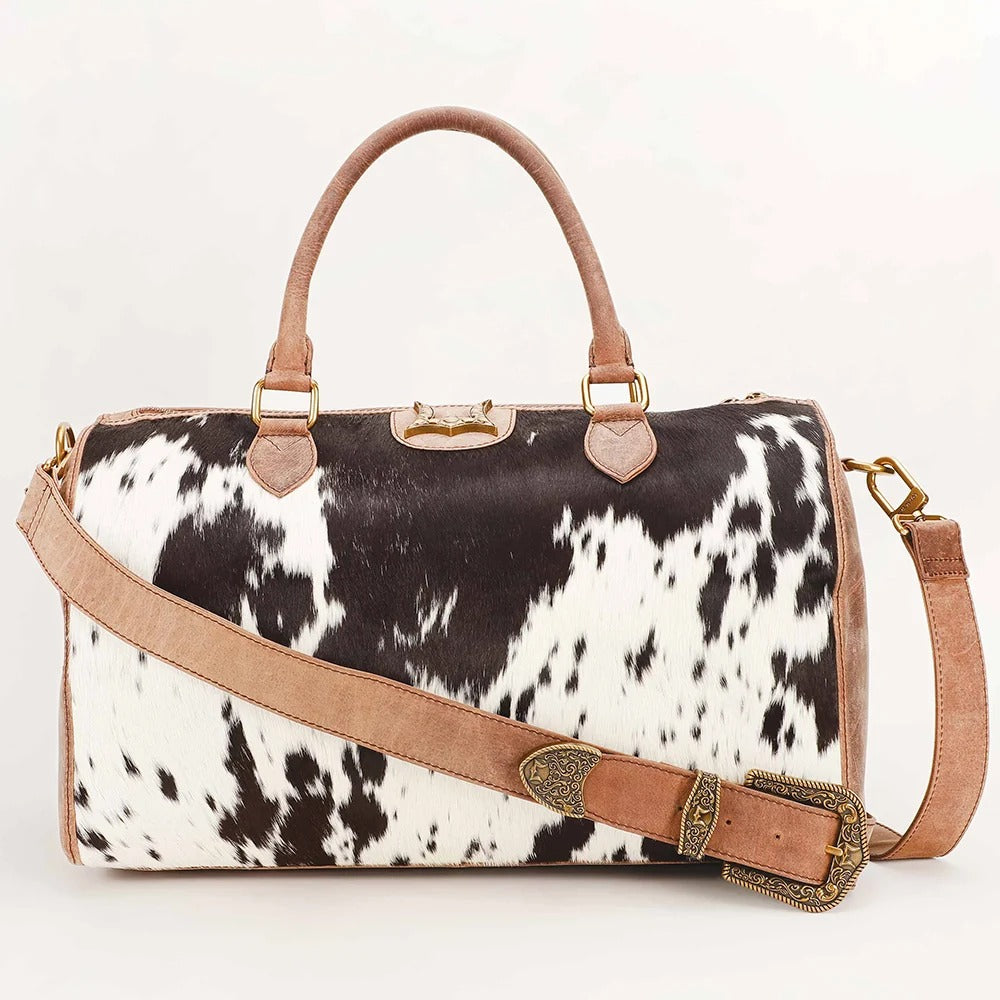 House of Hide handcrafted genuine leather black and white cow print handbag with brown leather straps showcased on a light gray studio background