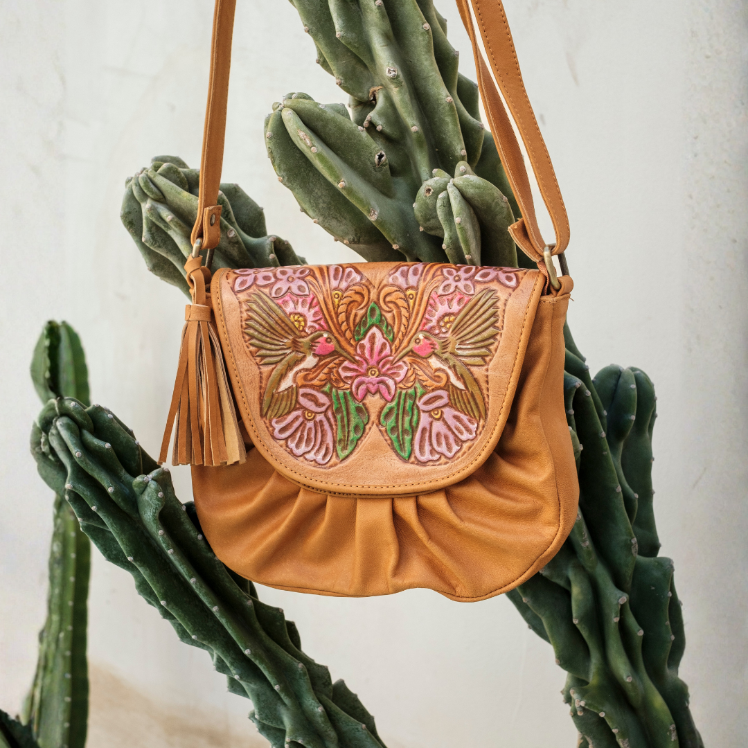 Magnolia Crossbody Bag from House of Hide in tan leather with floral embroidered flap being displayed hanging against white wall with green cactus
