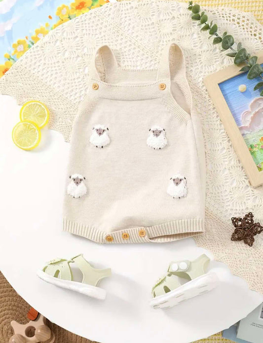 Neutral knit baby romper with embroidered lambs and wooden buttons, laid flat with toddler sandals