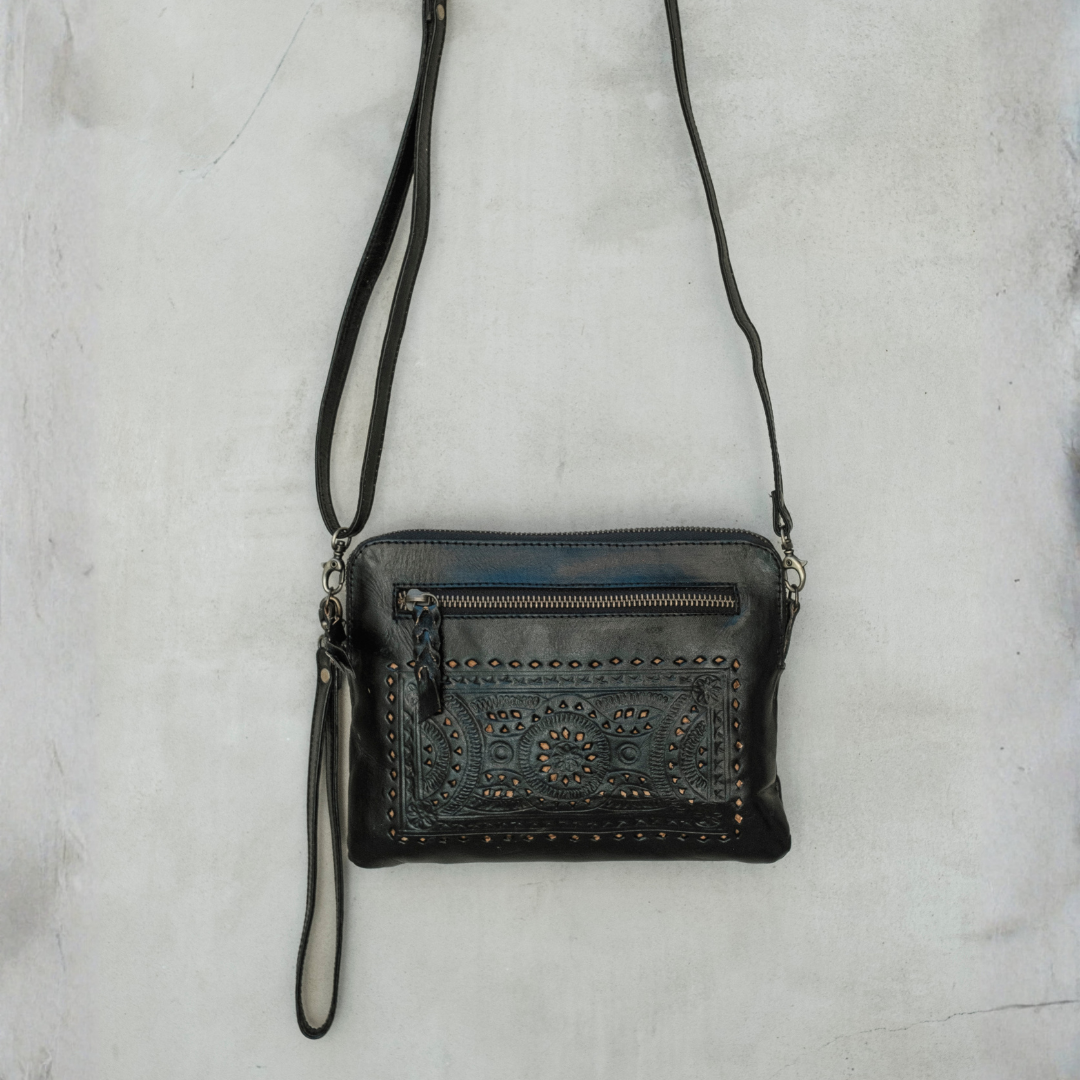 Nightshade Crossbody Bag from House of Hide in black leather with studded and embossed front zip pocket being displayed against textured light gray background