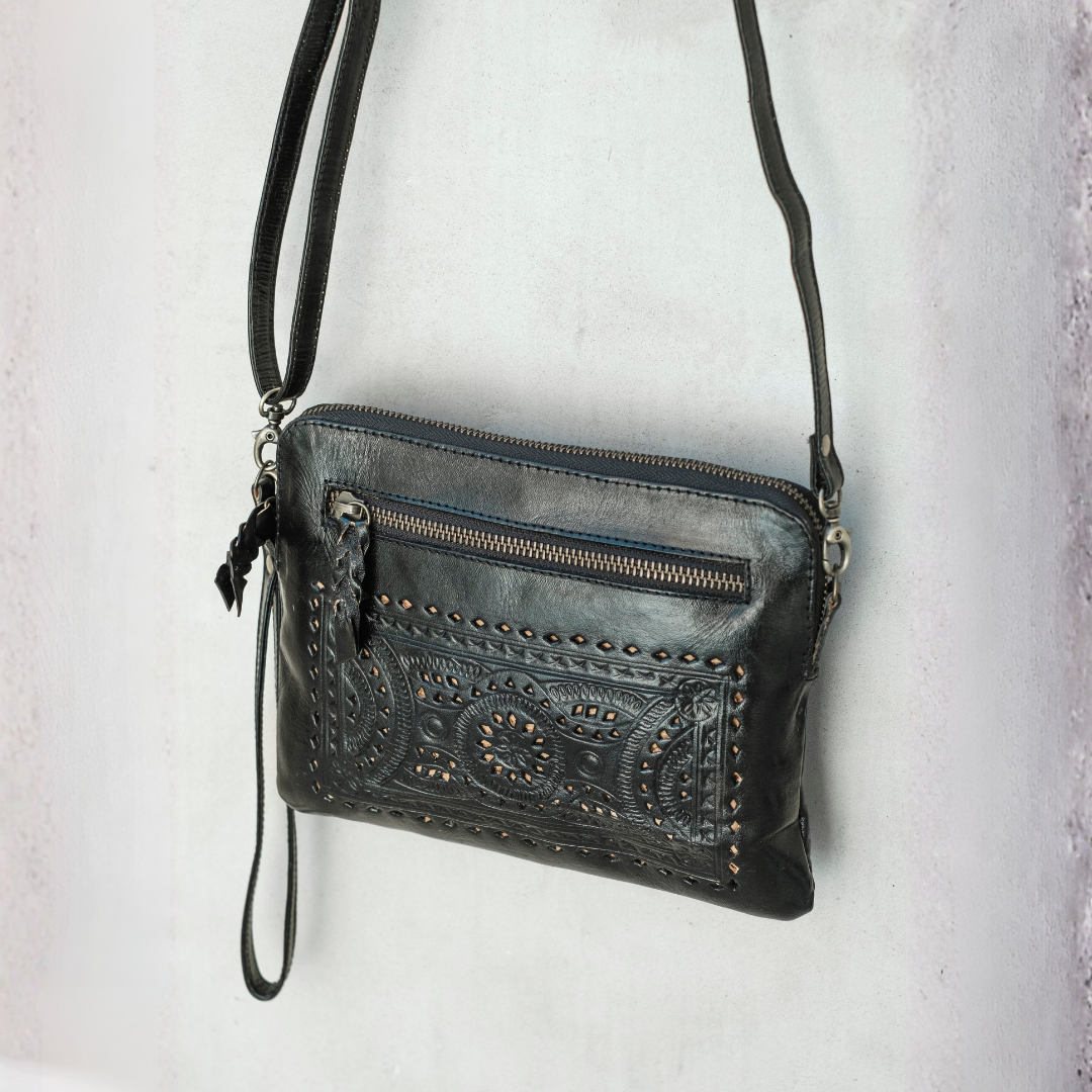 Nightshade Crossbody Bag from House of Hide in black leather with western-style tooling and studded trim, top zipper being displayed against light textured wall
