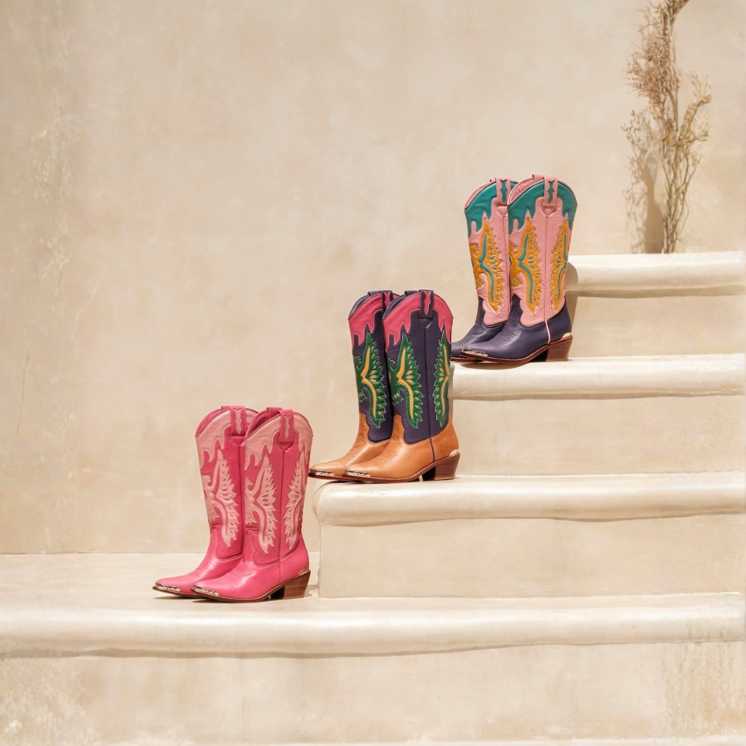 Three pairs of western cowboy boots in different colors and patterns, arranged on beige stone steps against a textured beige wall.