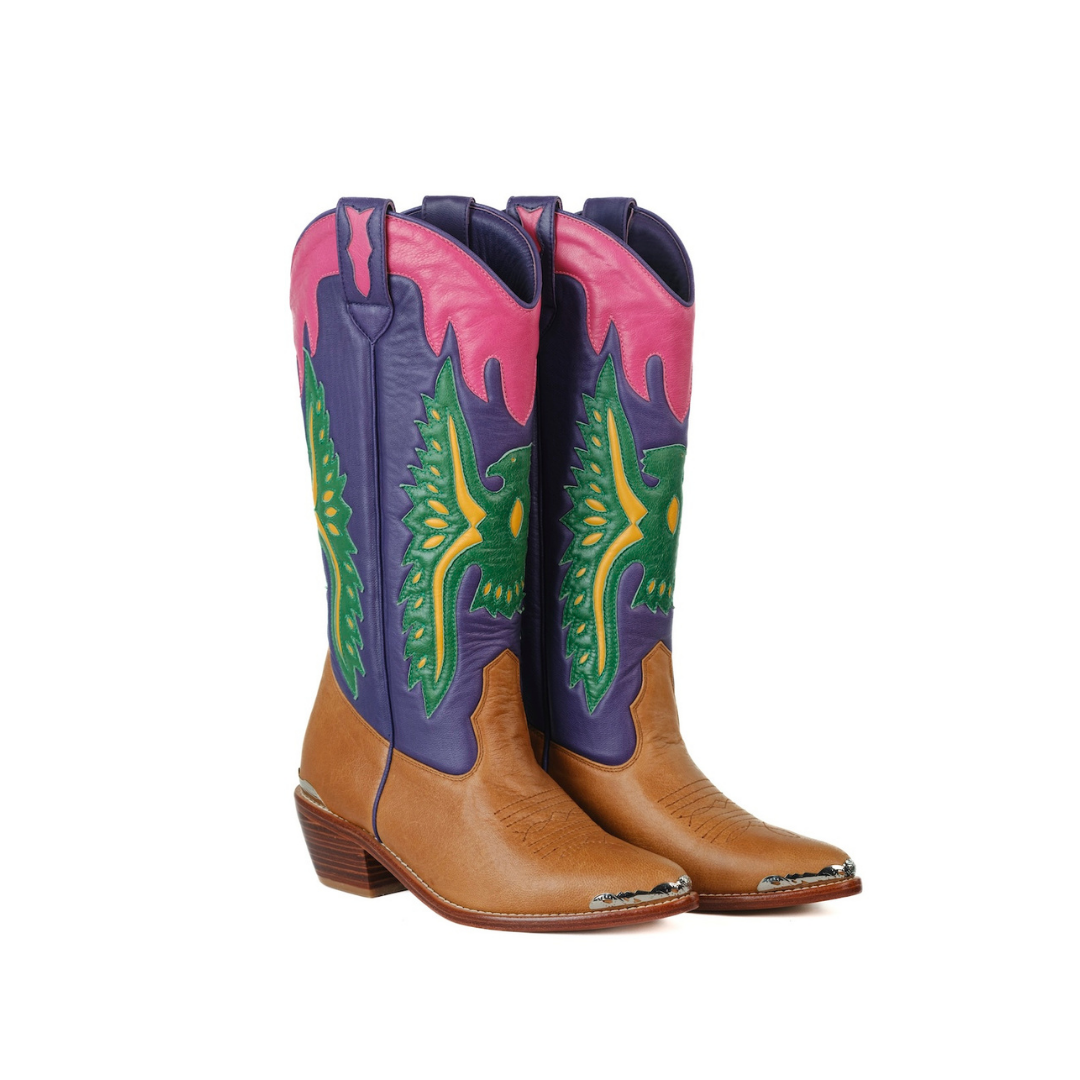 A pair of cowboy boots with tan leather lower sections, purple shafts, and vibrant pink, green, and yellow western embroidery, shown against a plain white background.
