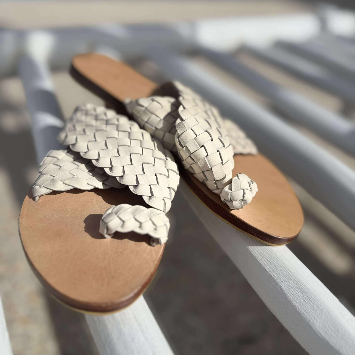 Pair of woven sandals with brown soles on a white metal surface.