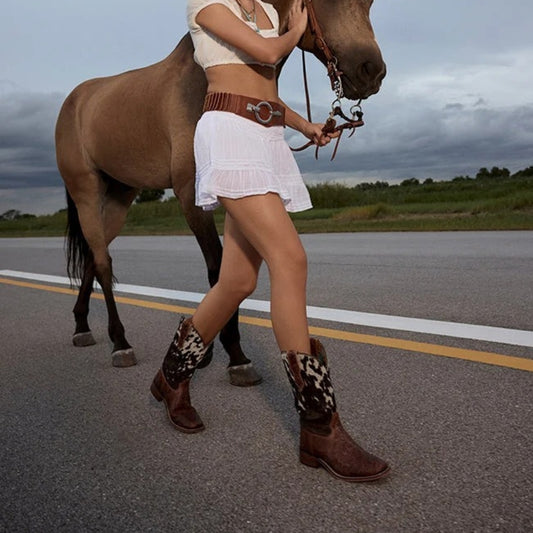 Savanna brown leather and speckled cowhide boots worn with a white skirt while walking beside a horse.