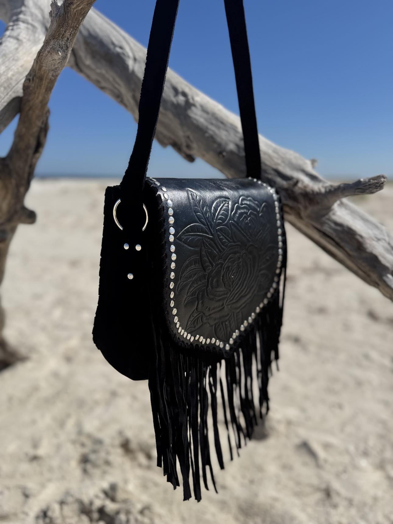 Shop the Ebony Wild – a black leather handbag with tassels and detailed stone embellishments.