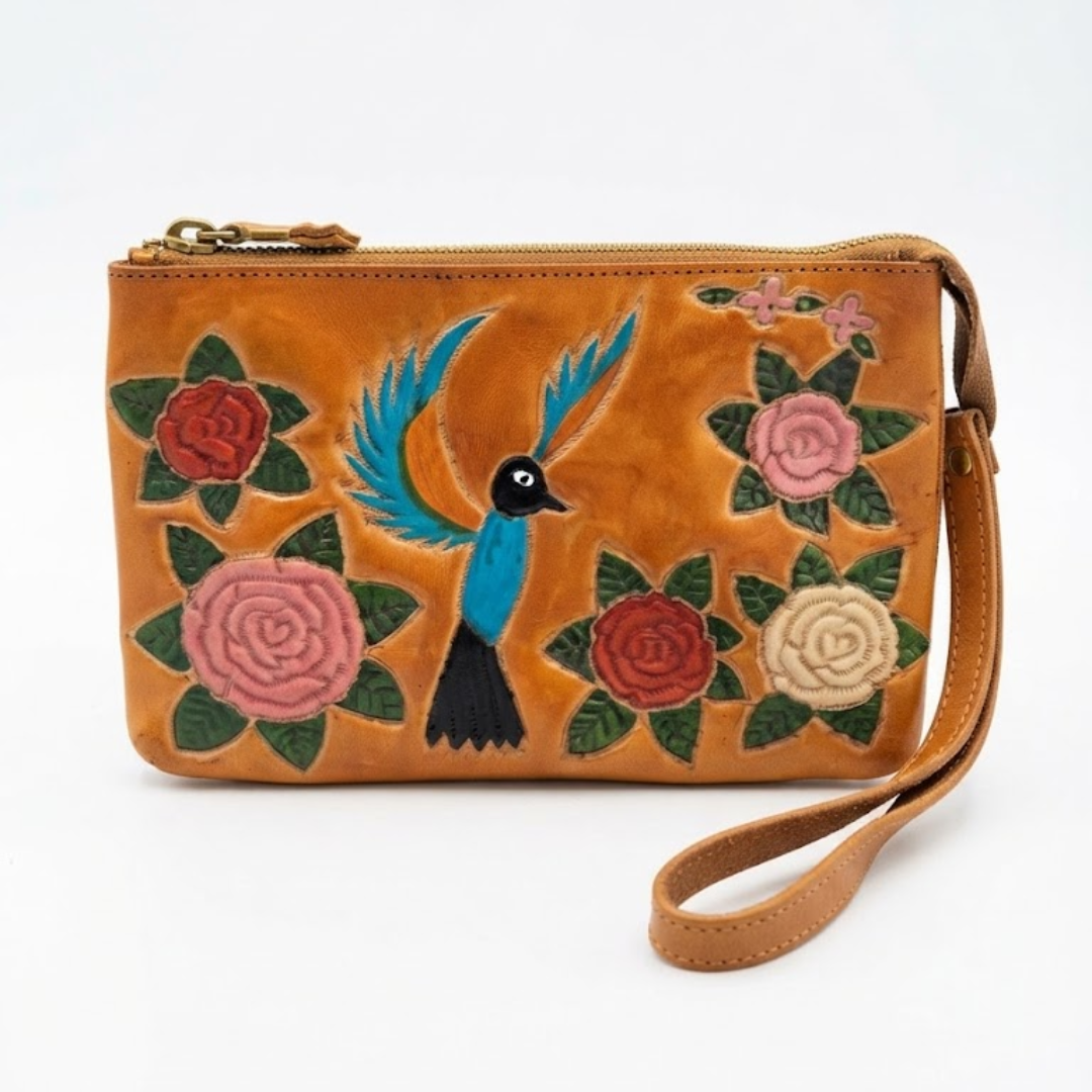 A tan leather wristlet clutch featuring hand-painted embroidery of a blue bird and pink, red, and cream roses with green leaves, shown on a white background.