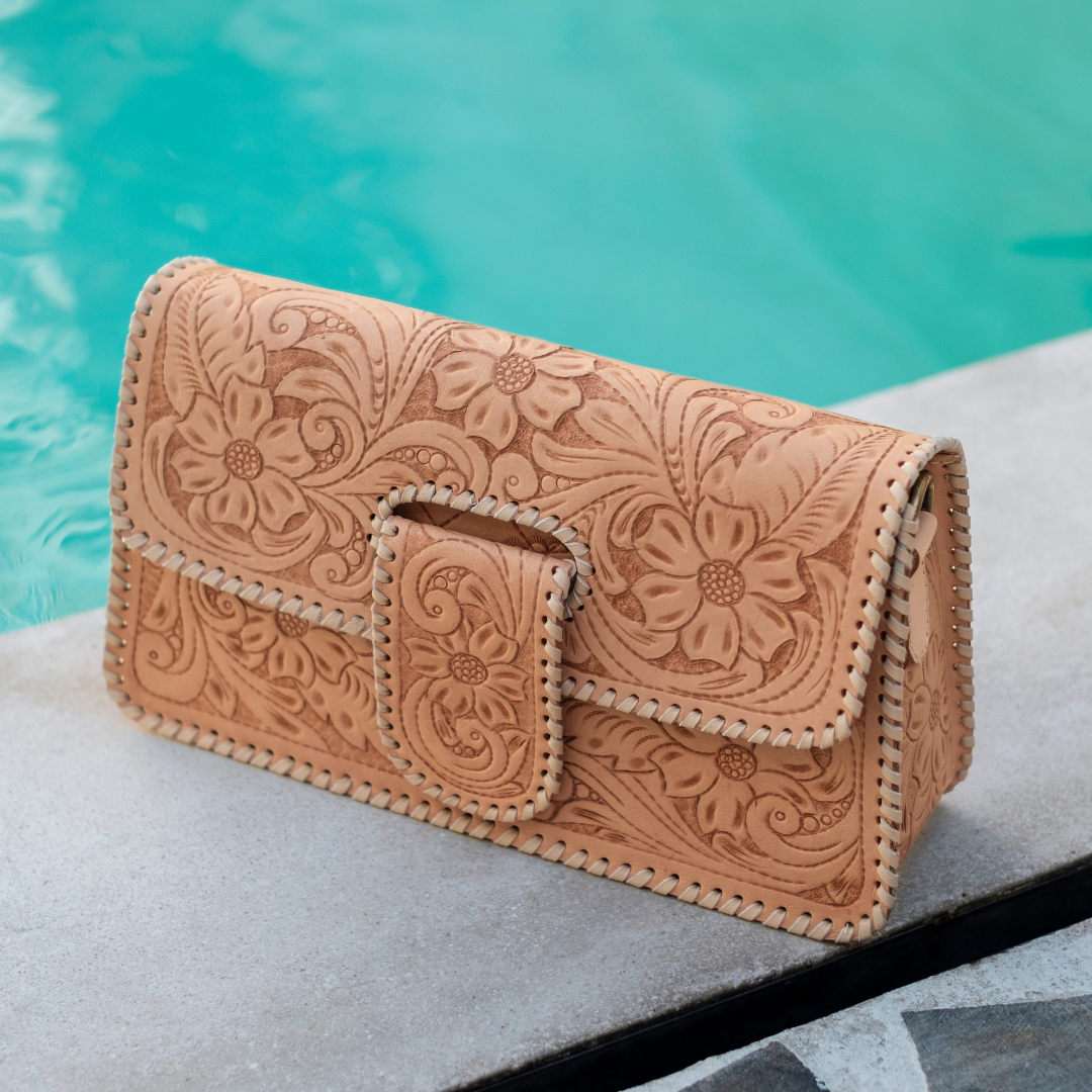Sunset Saddle Clutch Bag from House of Hide in tan tooled leather with floral embossing and whipstitched edges being displayed on concrete near swimming pool