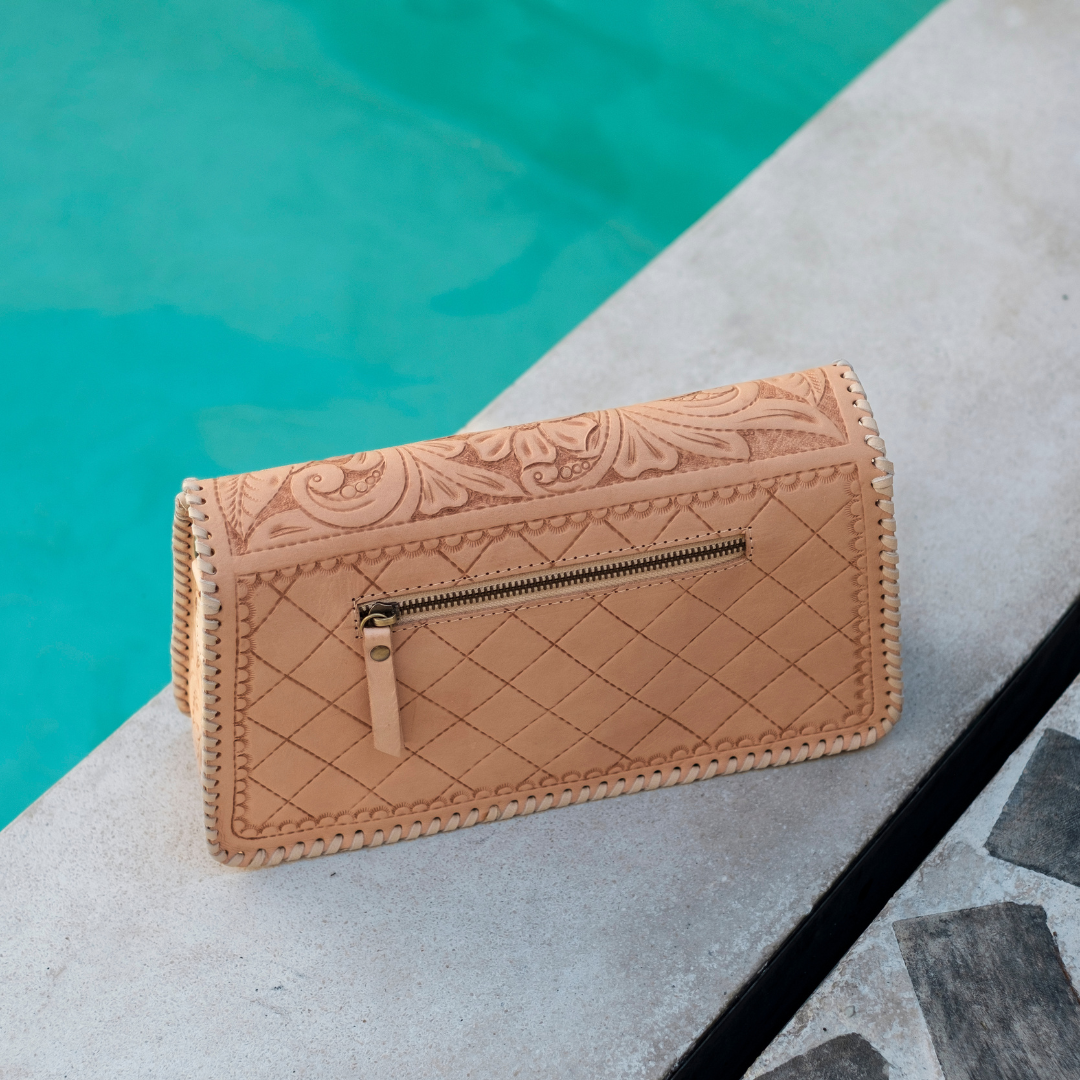 Sunset Saddle Clutch Bag from House of Hide in tan tooled leather with quilted front pocket and zipper being displayed on concrete poolside ledge with turquoise water