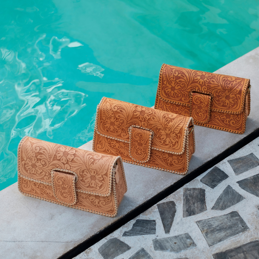 Sunset Saddle Clutch Bag from House of Hide in tan tooled leather arranged on stone poolside ledge with turquoise water background
