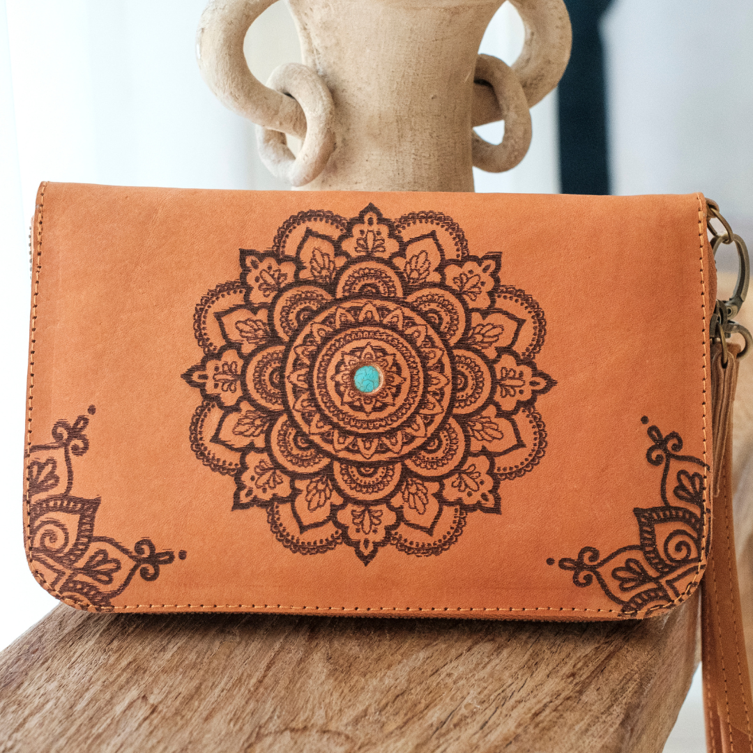 House of Hide Talisman Wallet in tan leather with brown mandala design and turquoise center stone being displayed on wooden surface with ceramic accent