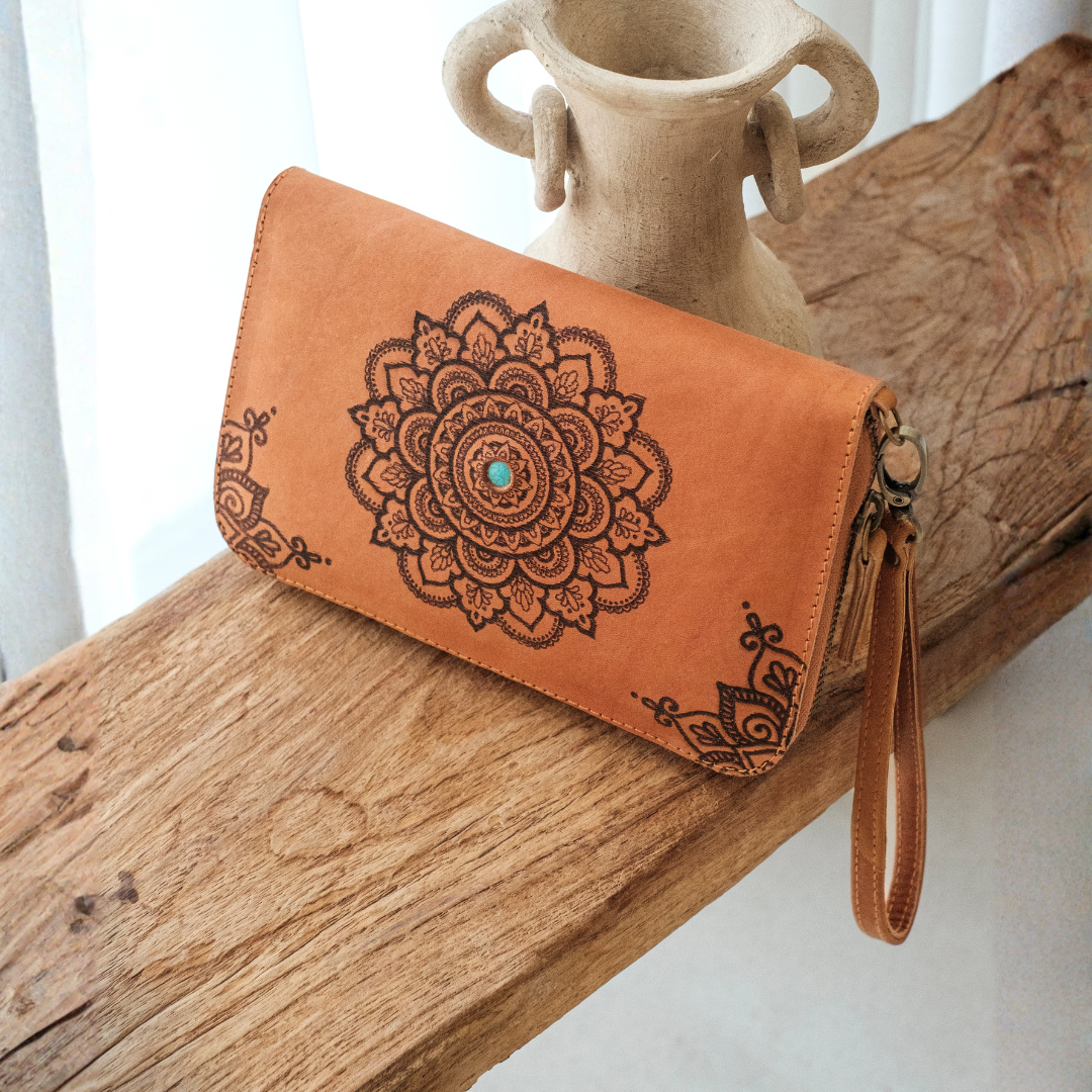 House of Hide Talisman Wallet in tan leather with laser-engraved mandala design and turquoise center accent being displayed on rustic wooden surface with ceramic vase