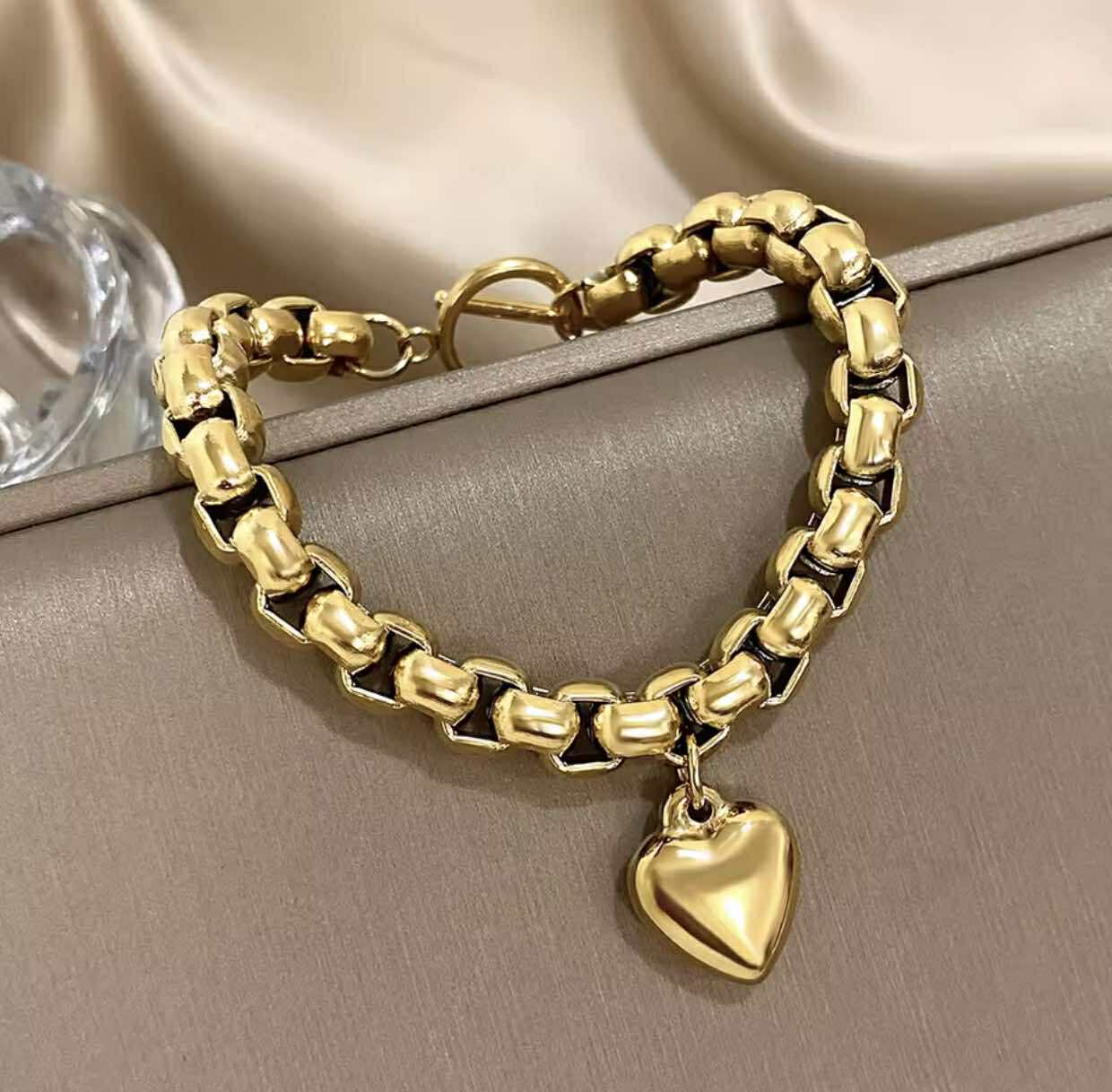 Waterproof gold bracelet with sculptural heart detail styled on soft fabric background