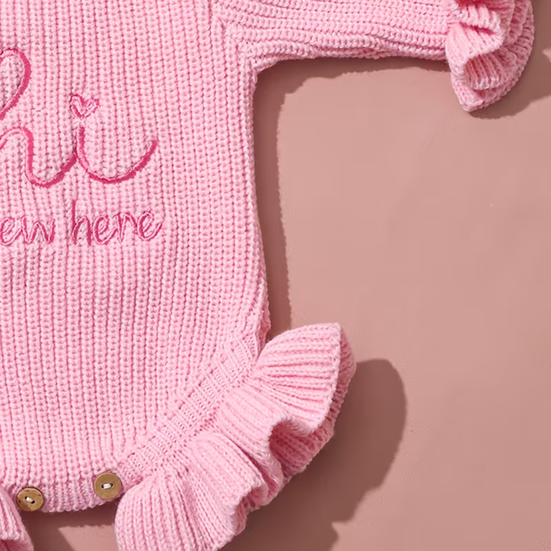 Welcome Baby Romper Set from House of Hide in soft pink chunky ribbed knit baby romper with hi I'm new here announcement embroidery, picture-perfect ruffled edges, snap button closure for easy changes, matching bold bow headband included as complete newborn photography set