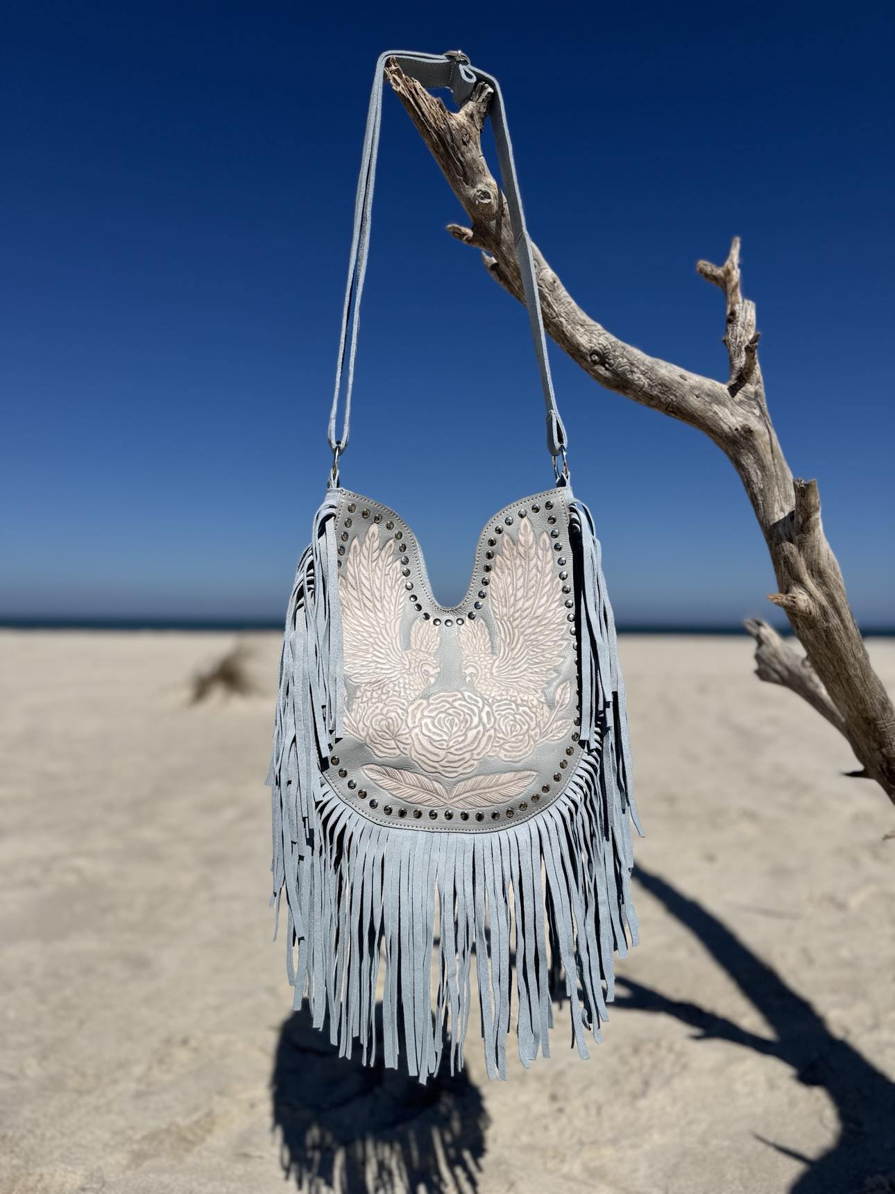 Western-style blue leather bag with hand-tooled details and fringe tassels, ideal for summer color analysis.