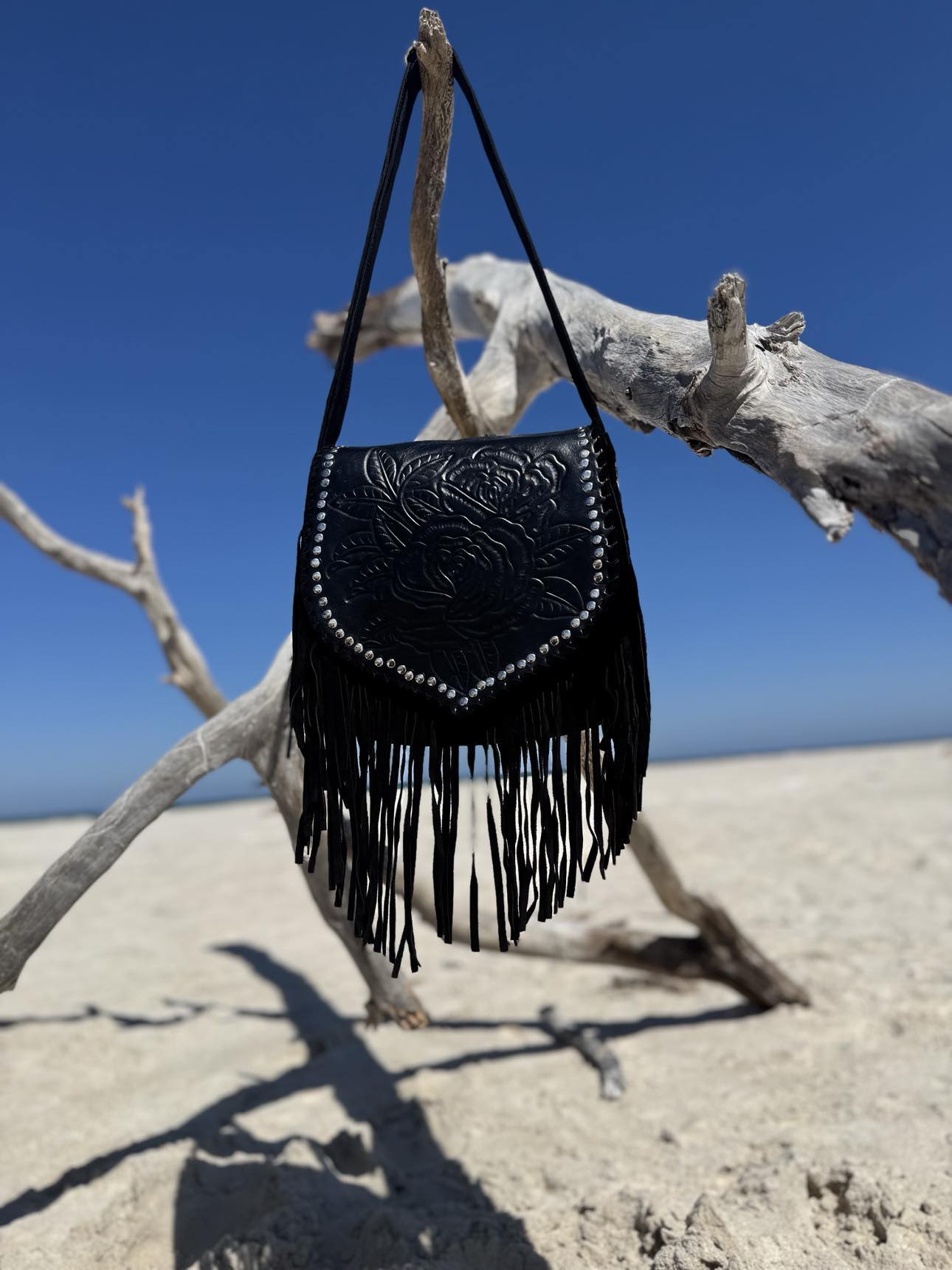 Western style black leather handbag with stone accents and intricate fringe for a boho-inspired look.