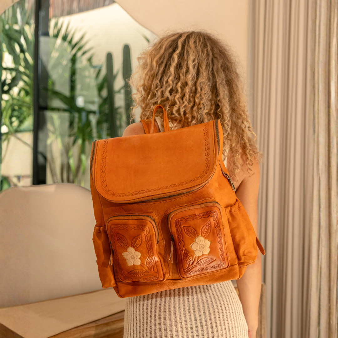 Wild Rose Leather Backpack from House of Hide in warm orange-brown suede with two front flap pockets featuring embossed floral designs being worn from behind by model in softly lit indoor room with curtains and greenery