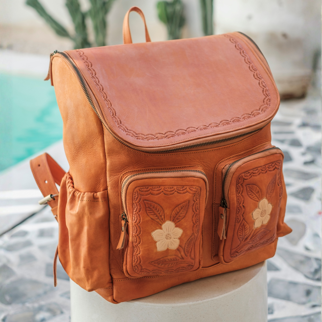 Wild Rose Leather Backpack from House of Hide in tan leather with floral embossed details and zippered pockets being displayed on white pedestal in outdoor setting