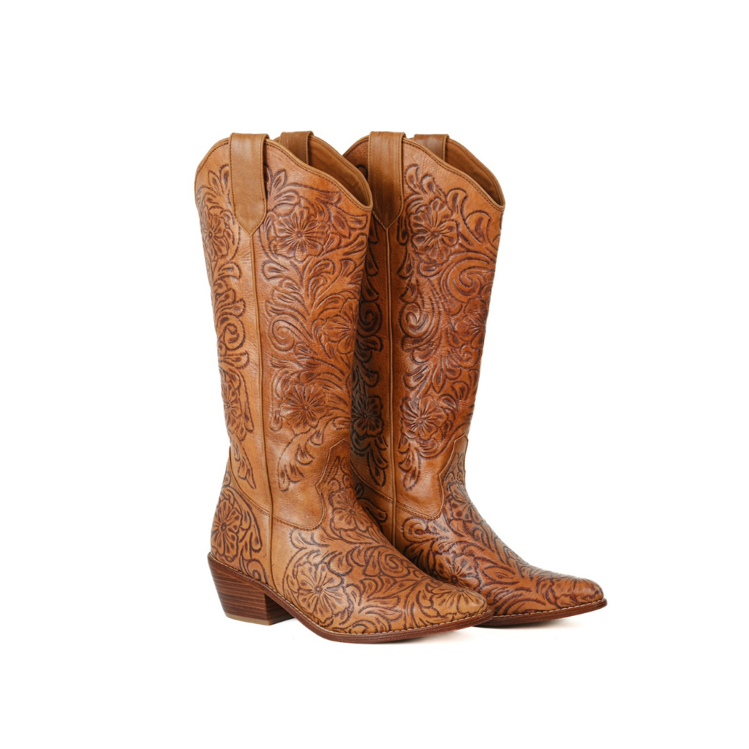 A pair of tan leather cowboy boots with intricate floral tooling, shown from a three-quarter angle against a plain white background.