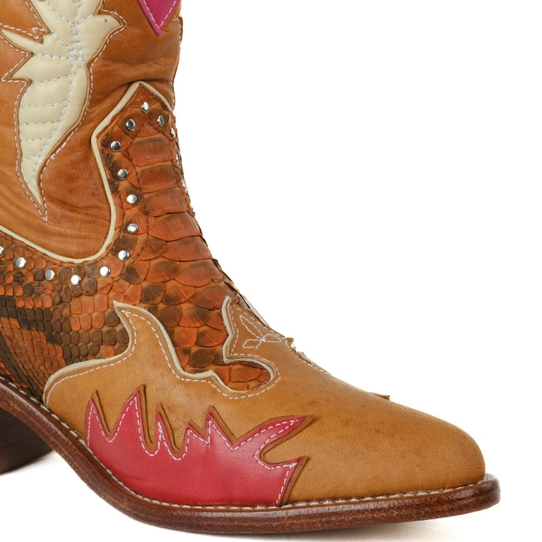 A close-up of a western boot featuring tan and brown leather panels, a red flame-like patch on the vamp, and silver studs, set against a plain white background.