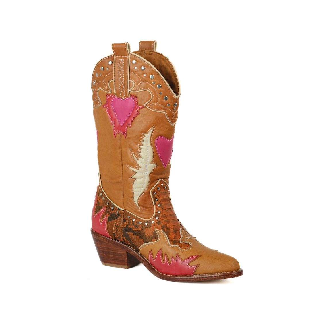 A single tan leather cowboy boot with pink heart-shaped patches, brown flame-patterned leather on the lower shaft and foot, and silver studs, shown against a plain white background.