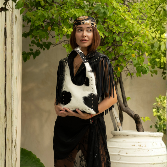Wrangler Cowhide Bag from House of Hide in black and white cow-print cowhide leather being held by model in outdoor garden setting with potted tree