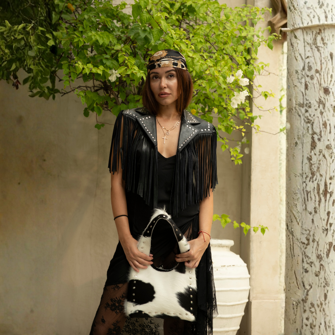 Wrangler Cowhide Bag from House of Hide in black and white cowhide leather being held by model outdoors against green foliage and stone wall background