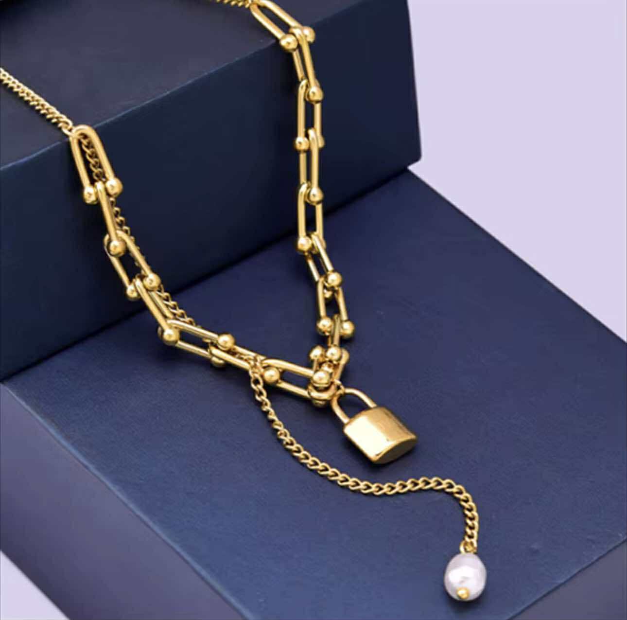 Close-up of chunky gold chain with vintage lock and hanging pearl detail