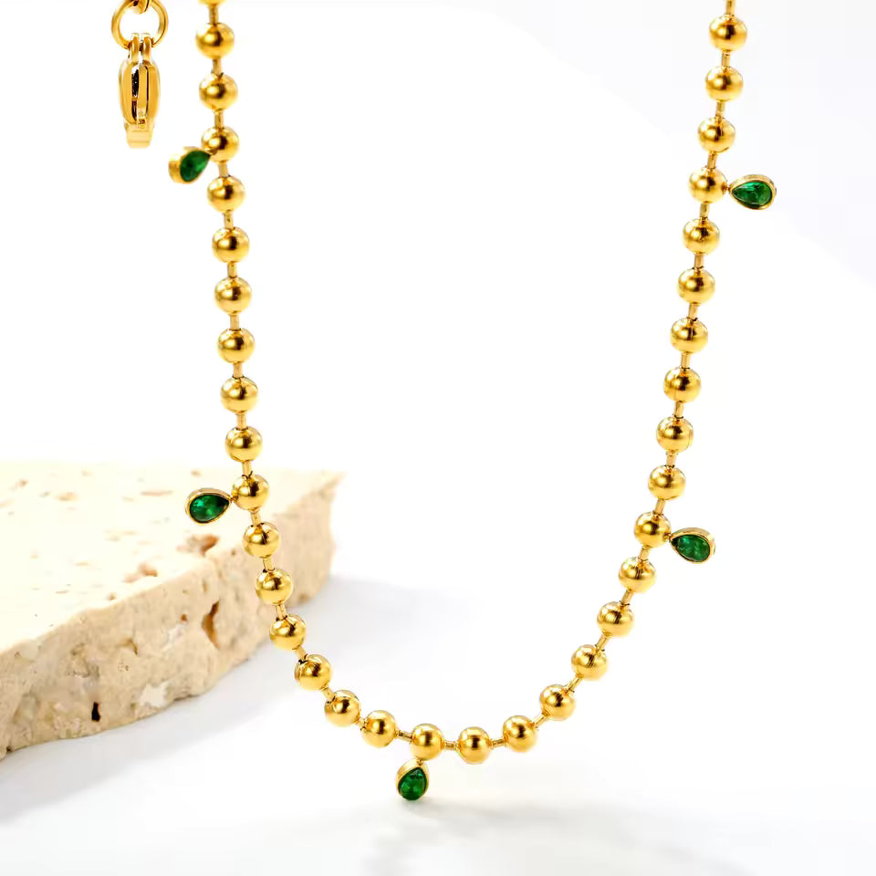 Gold necklace with green gemstones on a white background