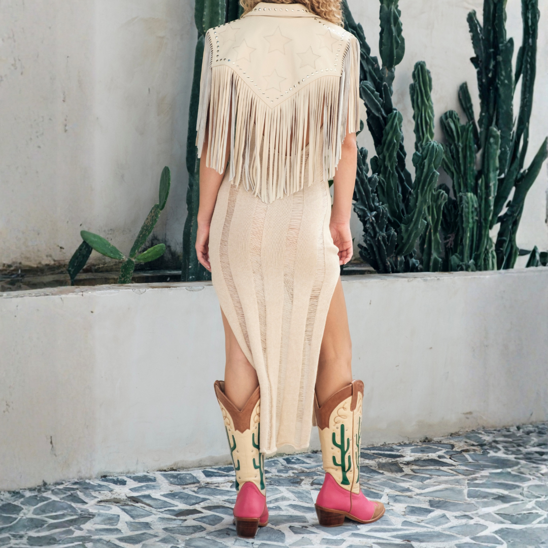 Person wearing a beige fringe dress and cowboy boots with cacti in the background